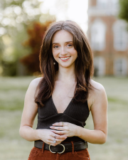 Woman with dark brown hair wearing a black tanktop in front of a nature background